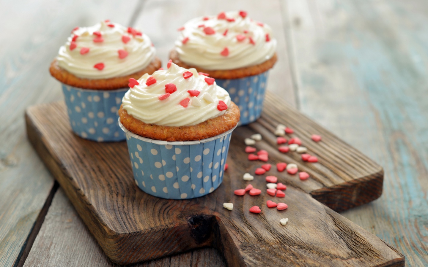 Три кекса со сливками украшены сердечками стоят на разделочной доске