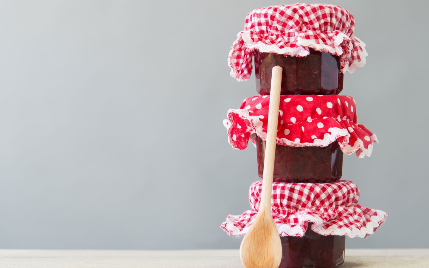 Три баночки варенья с деревянной ложкой на сером фоне