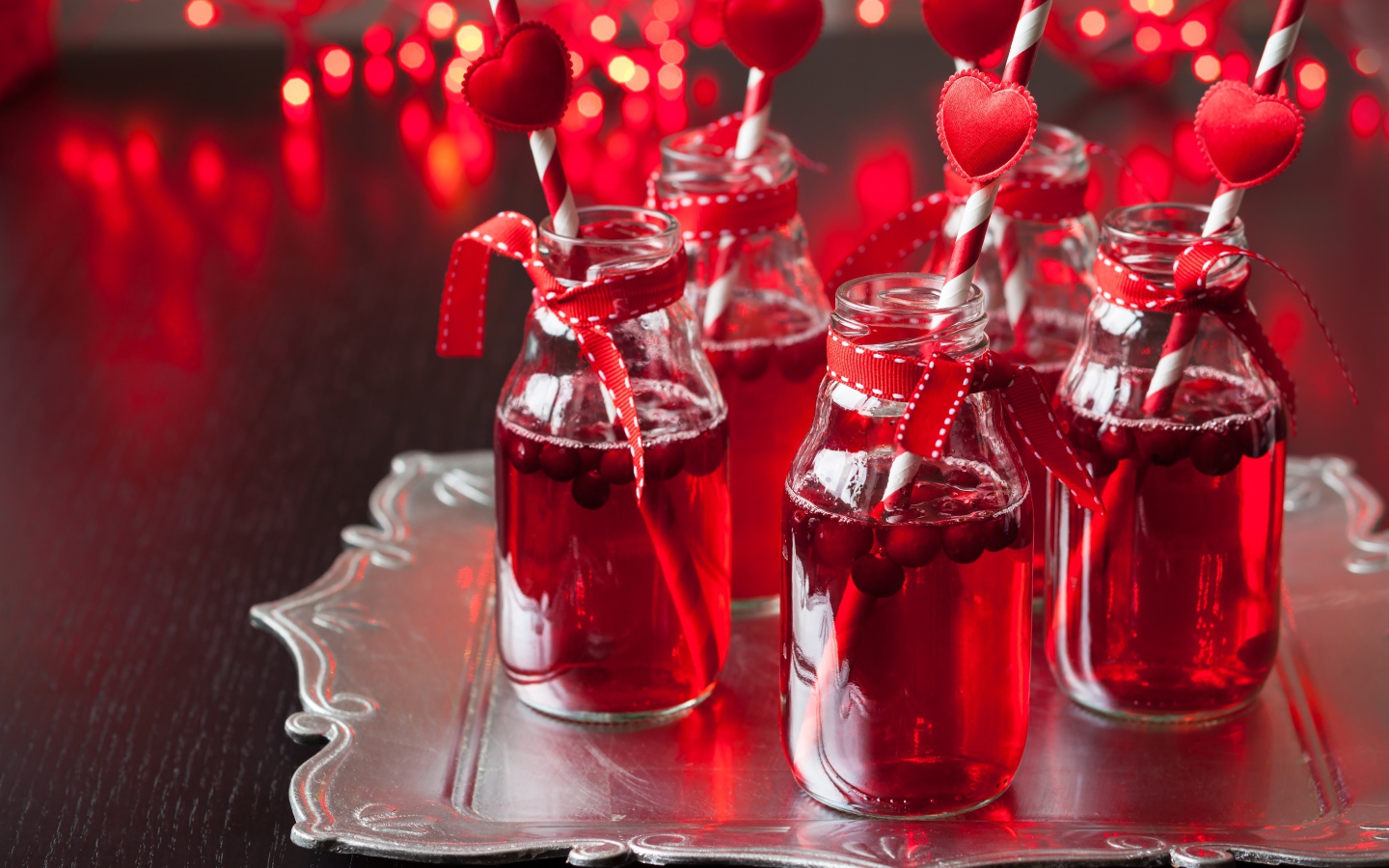 Вкусный напиток с клюквой в стеклянных бутылках на столе с трубочками