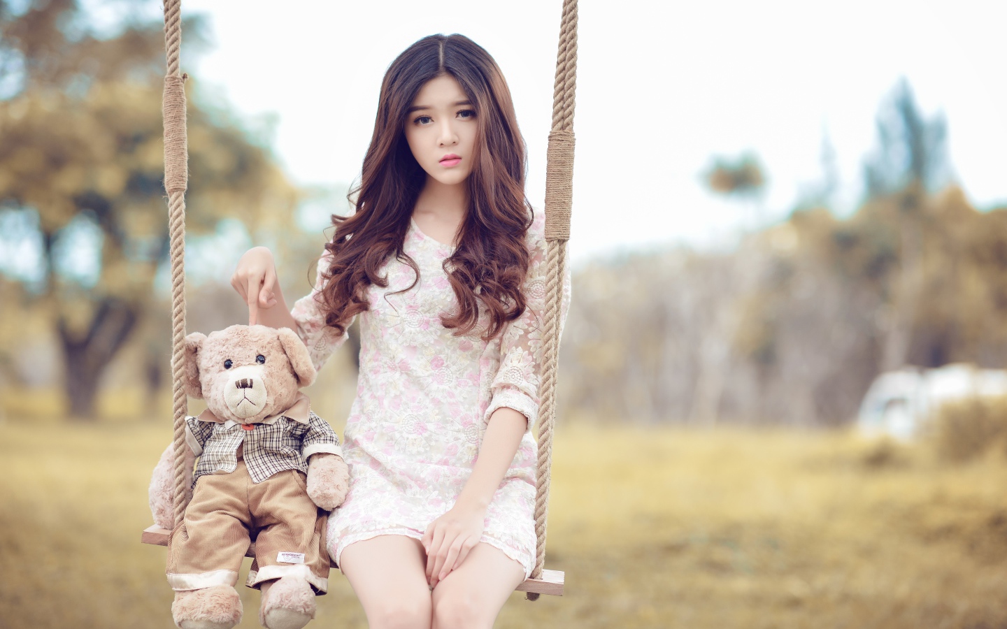 Asian girl sitting on a swing with a teddy bear.