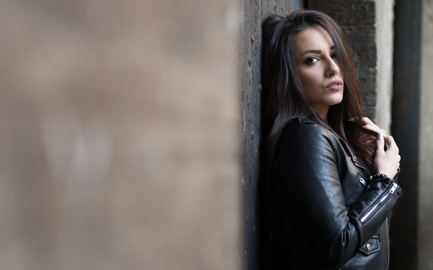 Красивая  брюнетка в кожаной куртке стоит у стены