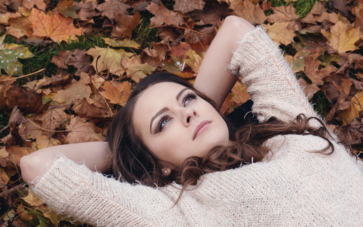 Красивая девушка в свитере лежит на опавших листьях 