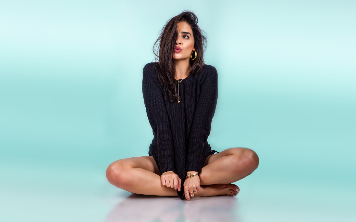 Красивая девушка сидит в черном свитере на голубом фоне