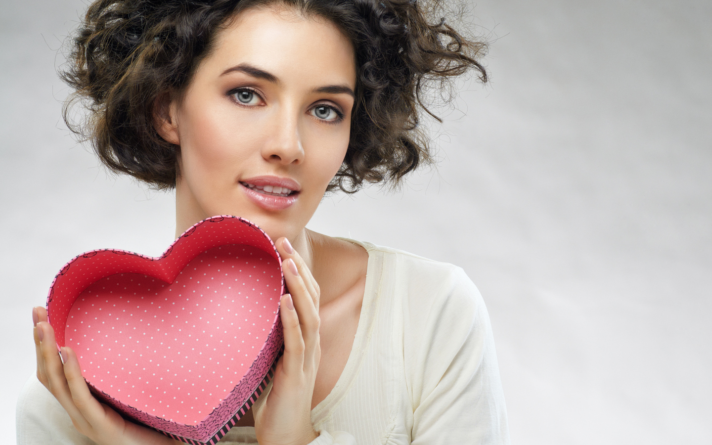 Красивая девушка с коробкой в форме сердца в руках на сером фоне