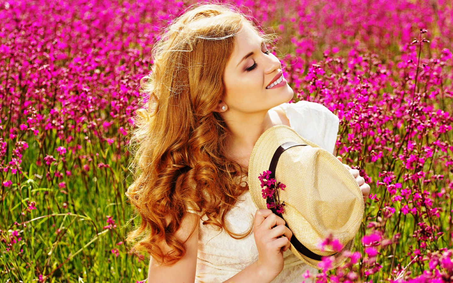 Красивая девушка с шляпой в руках на поле с розовыми цветами