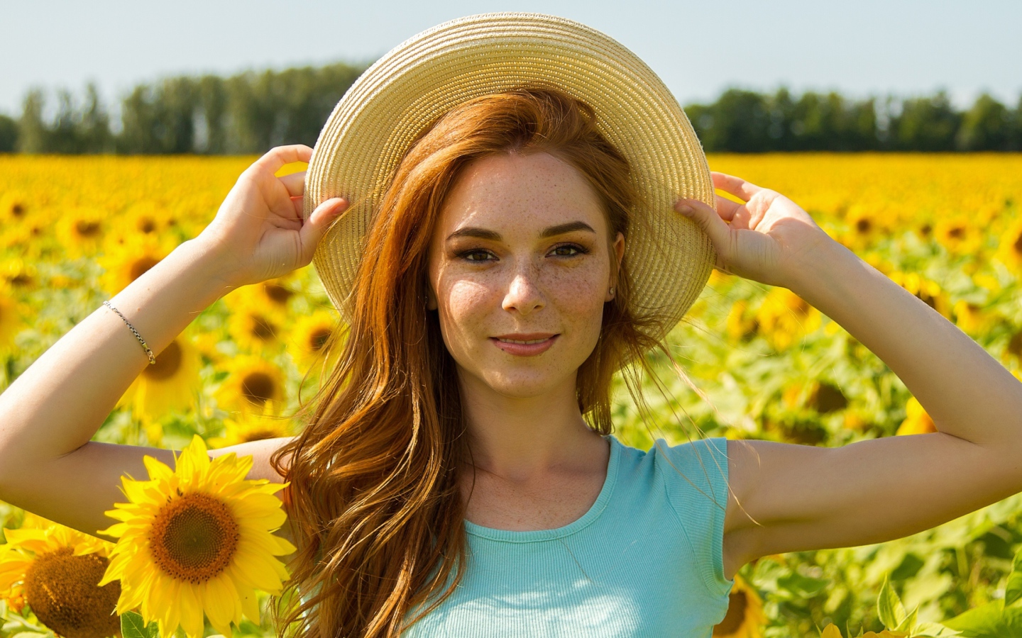 Красивая рыжеволосая девушка в шляпе на поле с подсолнухами 