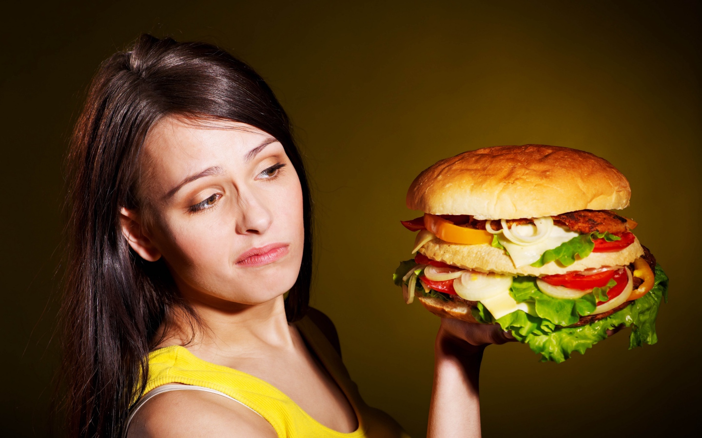 Недовольная девушка с большим гамбургером в руках 