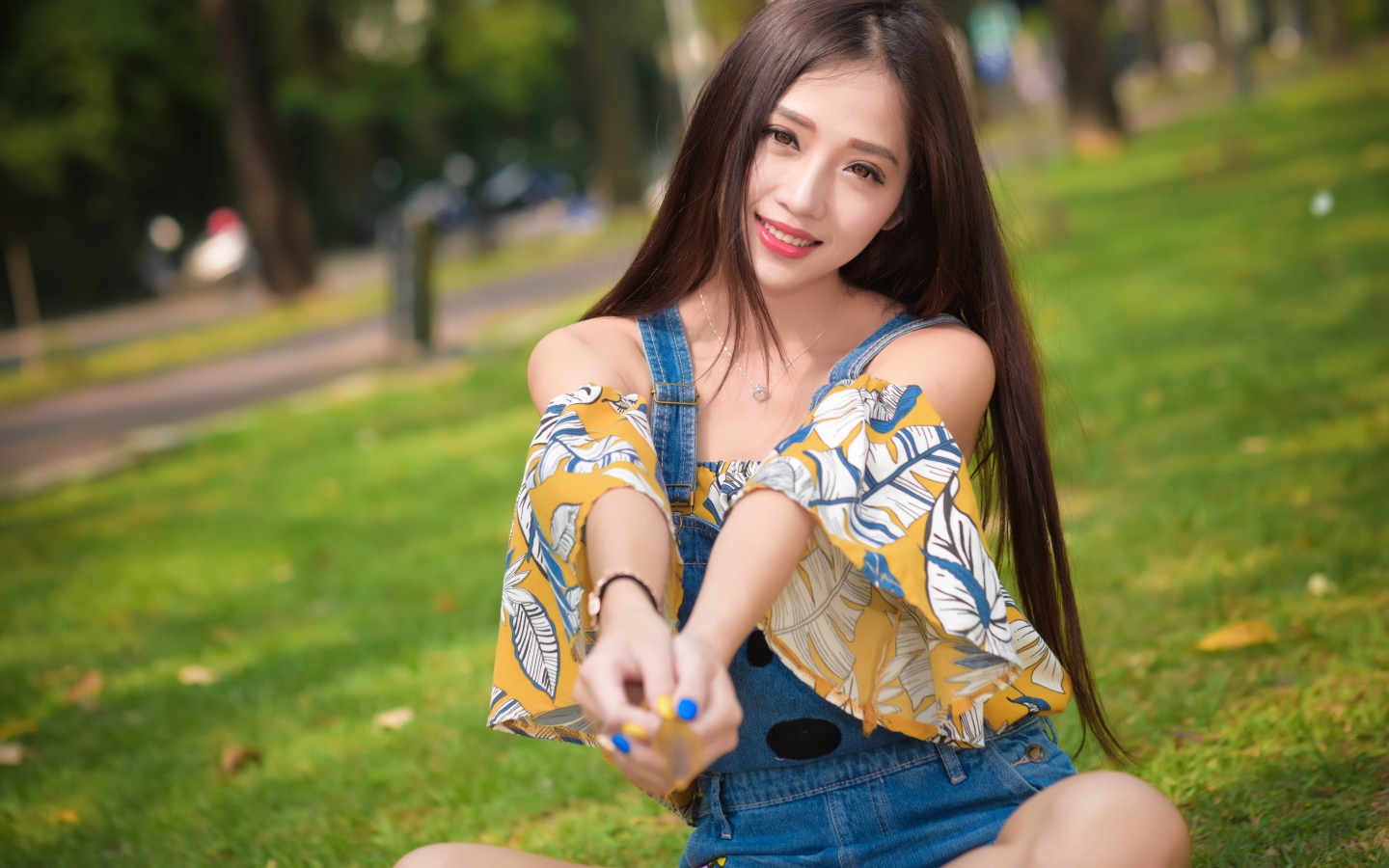 Улыбающаяся девушка азиатка сидит на траве