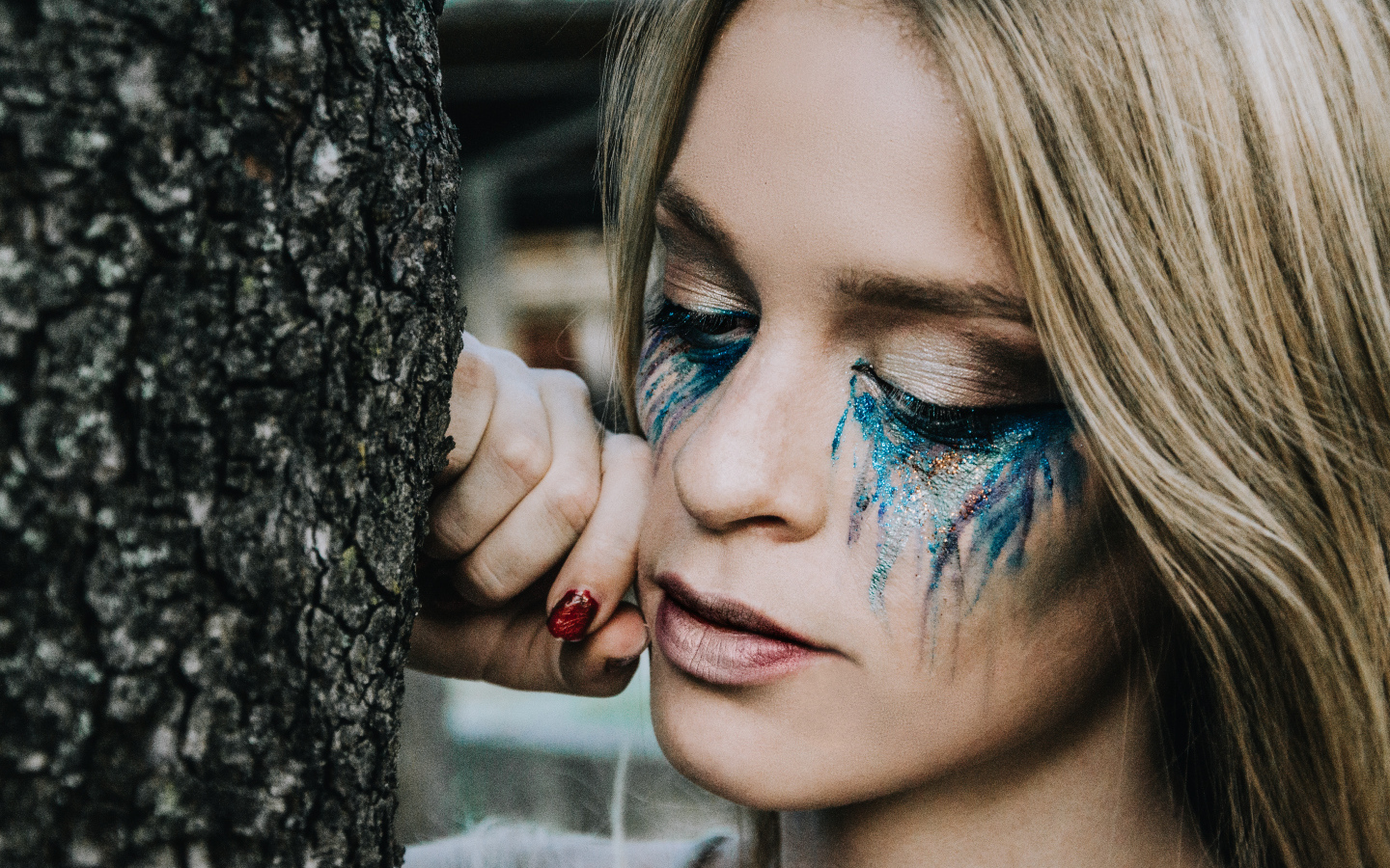 Заплаканная блондинка стоит у дерева