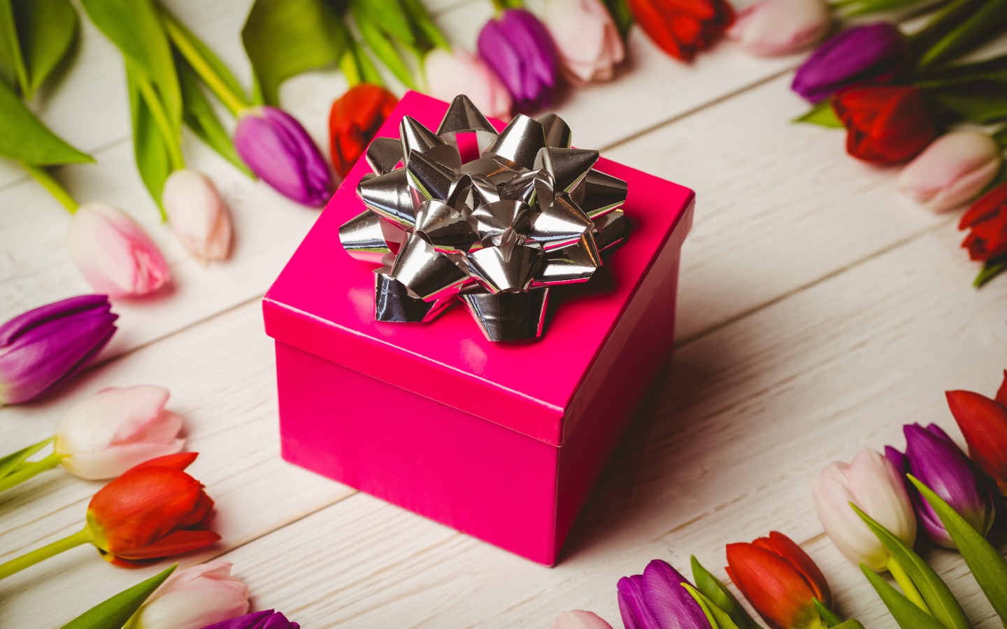 Красная коробка с подарком на столе с тюльпанами