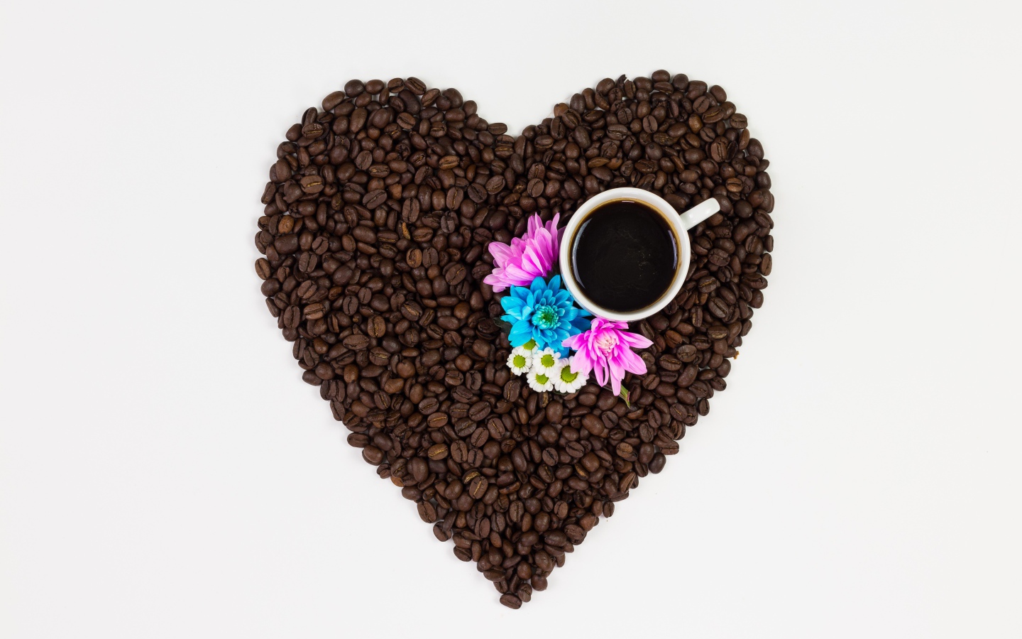 Сердце из кофейных зерен с чашкой на белом фоне