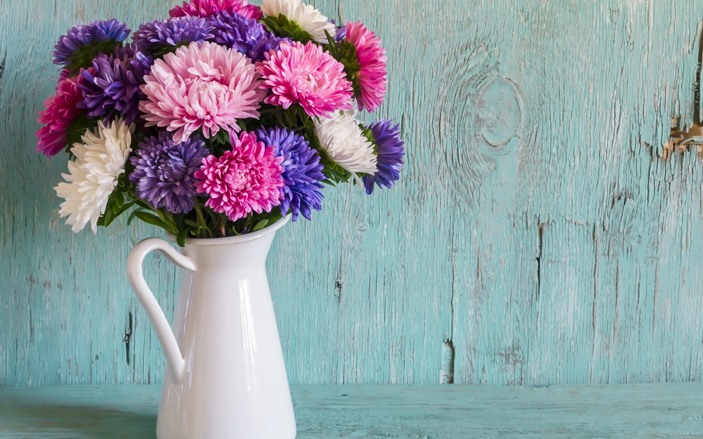 Разноцветные астры в вазе на деревянном фоне