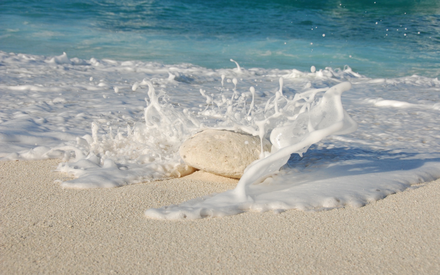 Белые морские волны бьются об камень на желтом песке