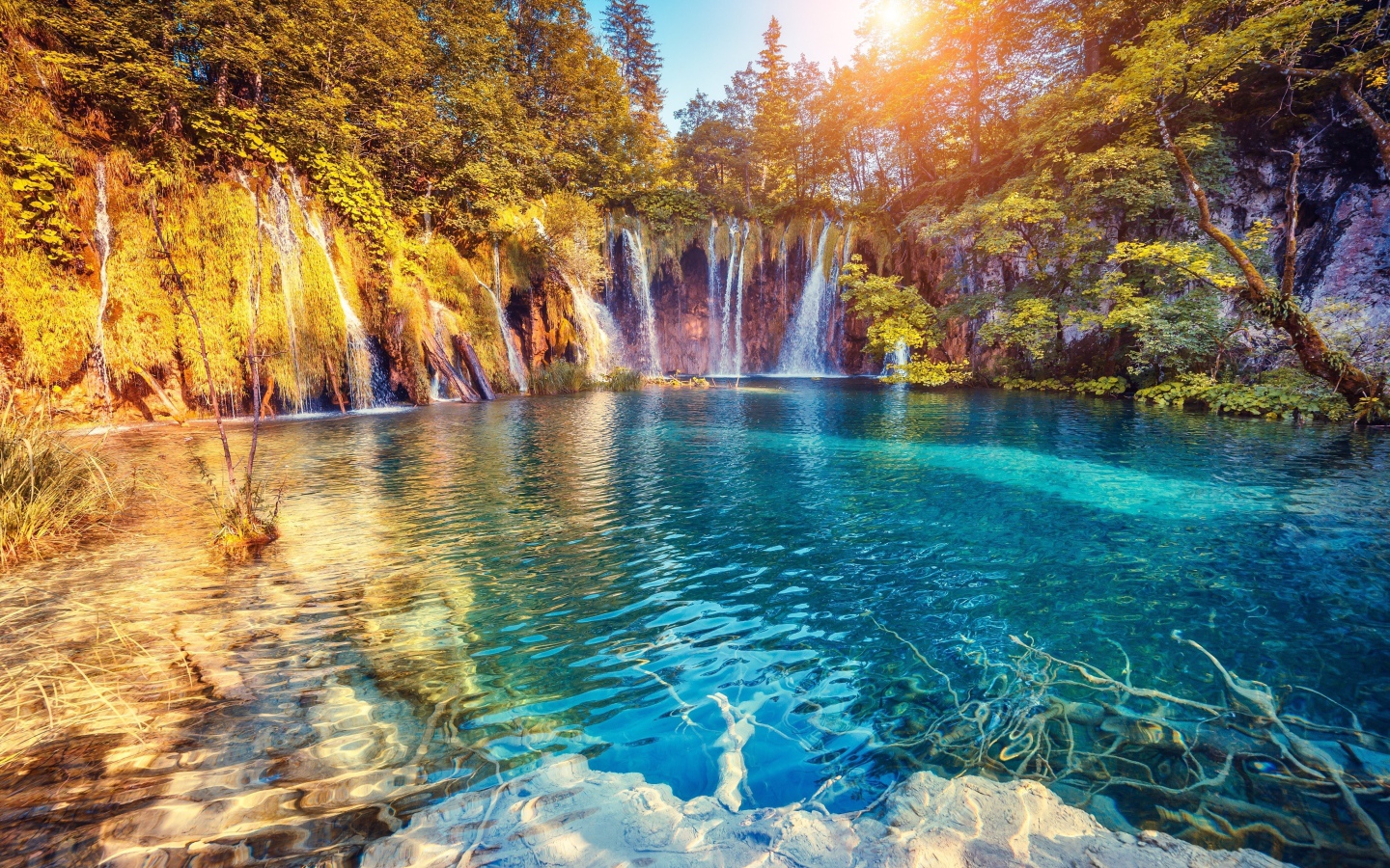 Водопад в лучах солнца стекает со скалы в реку