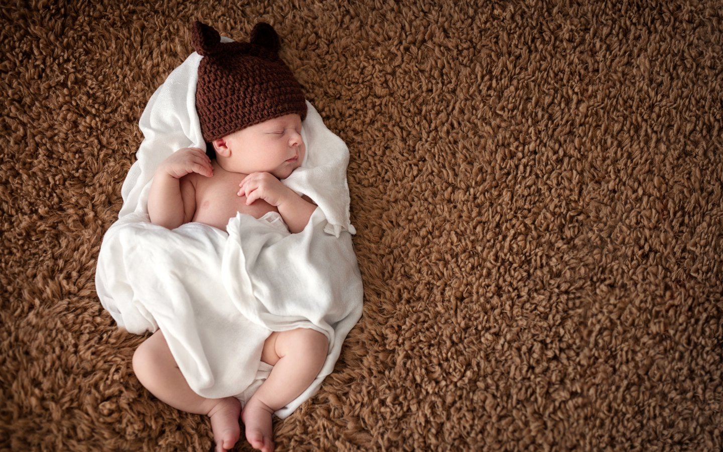 Грудной ребенок в вязаной шапке  спит в белом покрывале 