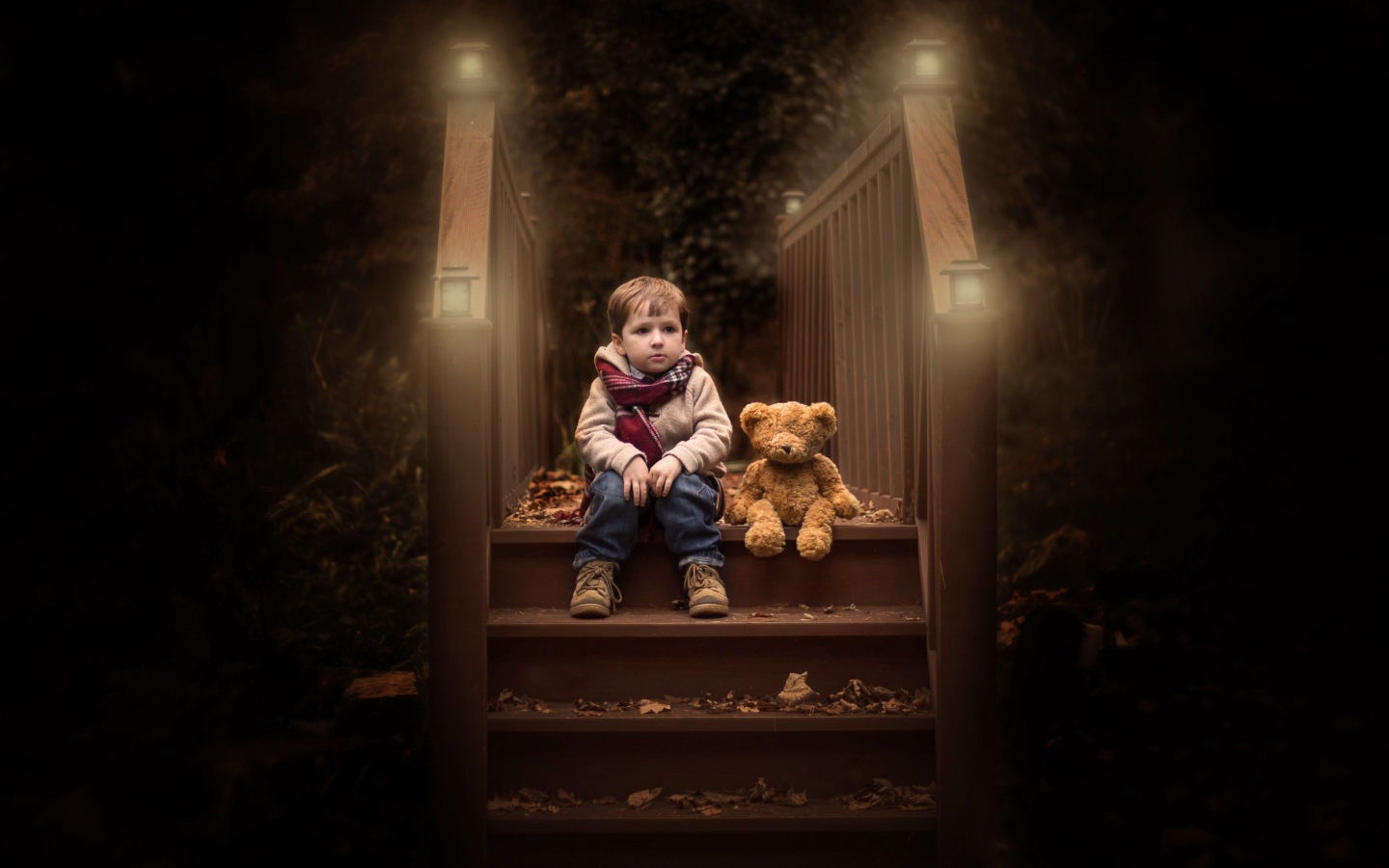 Маленький мальчик сидит с игрушечным мишкой на ступеньках