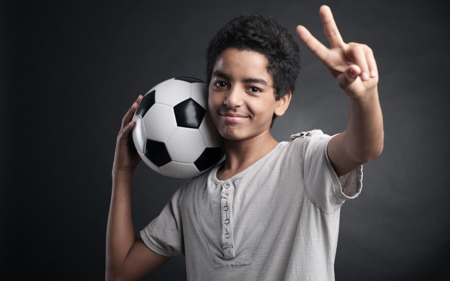 Мальчик с футбольным мячом на плече на сером фоне