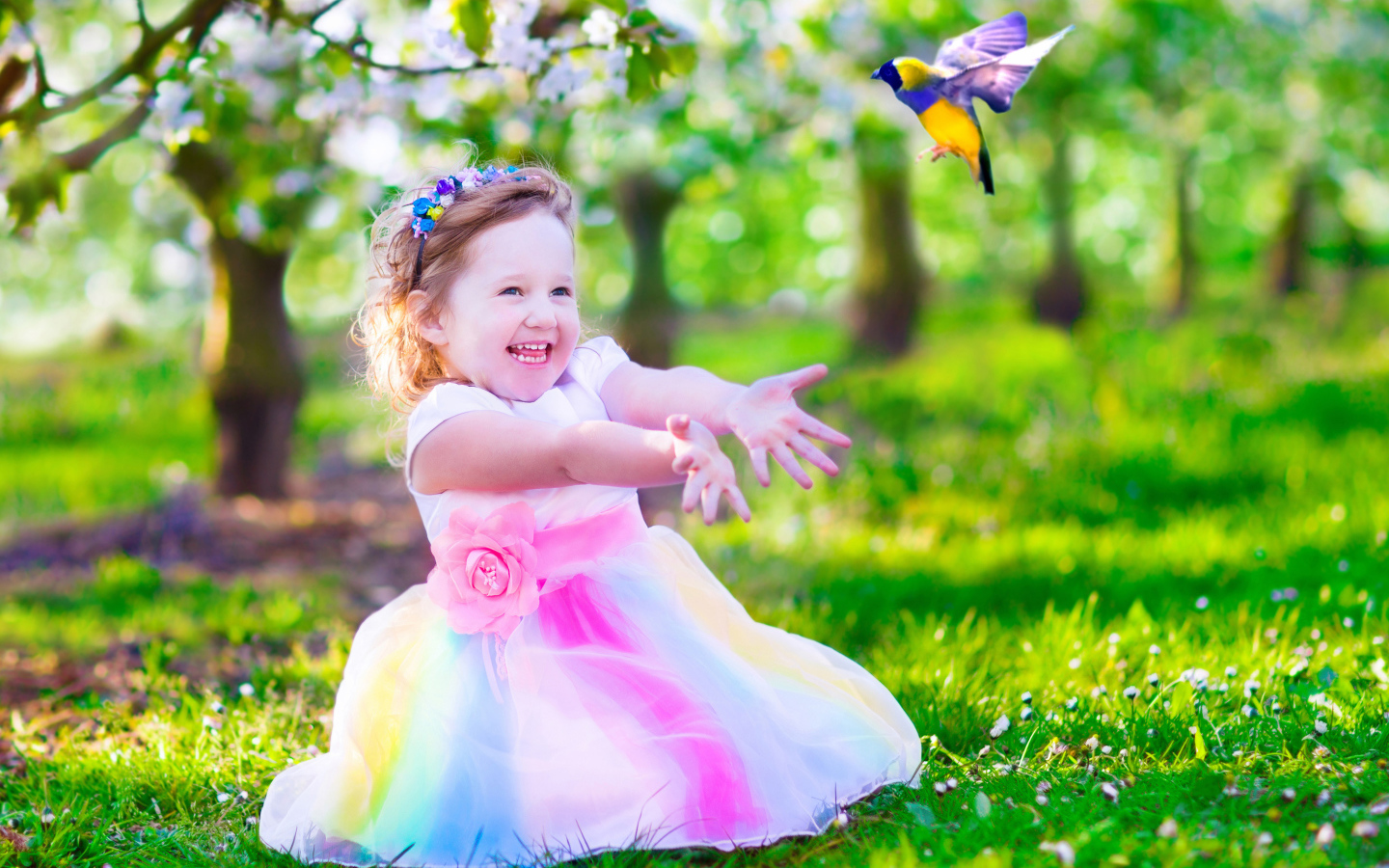 Смеющаяся маленькая девочка в красивом платье на зеленой траве
