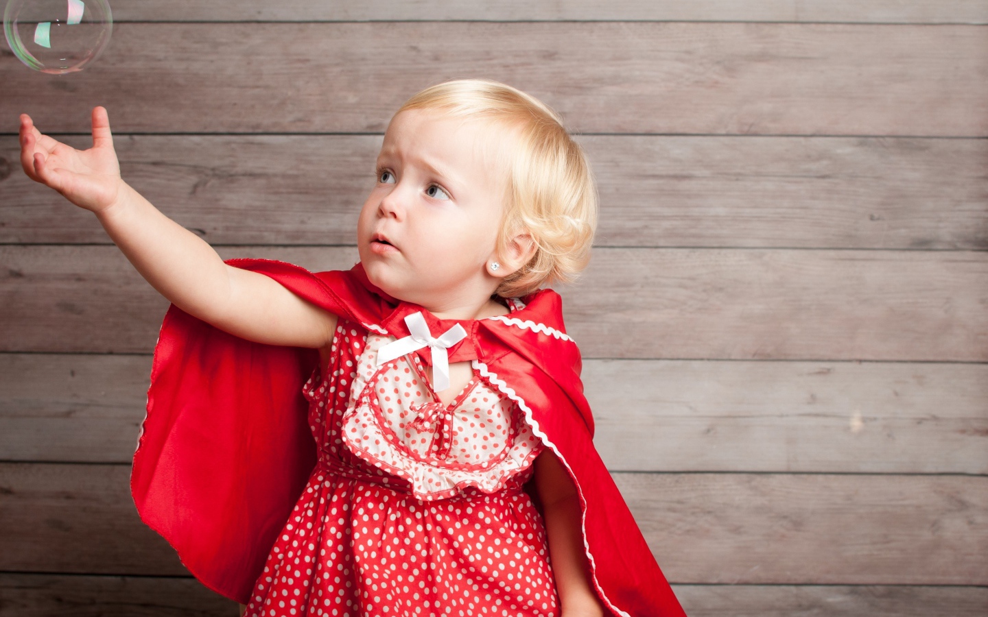 Маленькая девочка в красном платье ловит мыльный пузырь