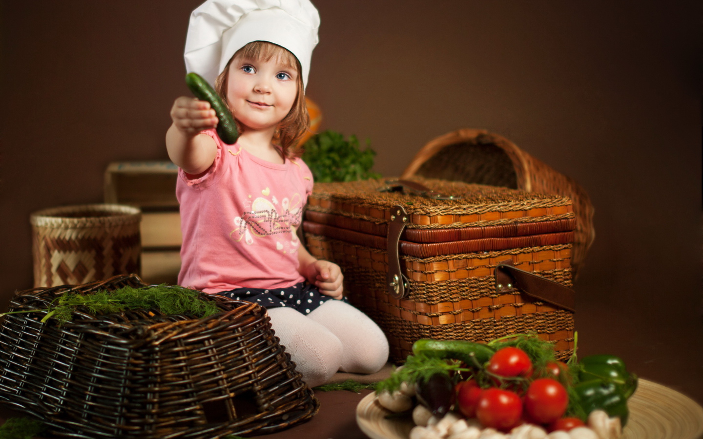 Маленькая девочка сидит на столе с корзинами и овощами