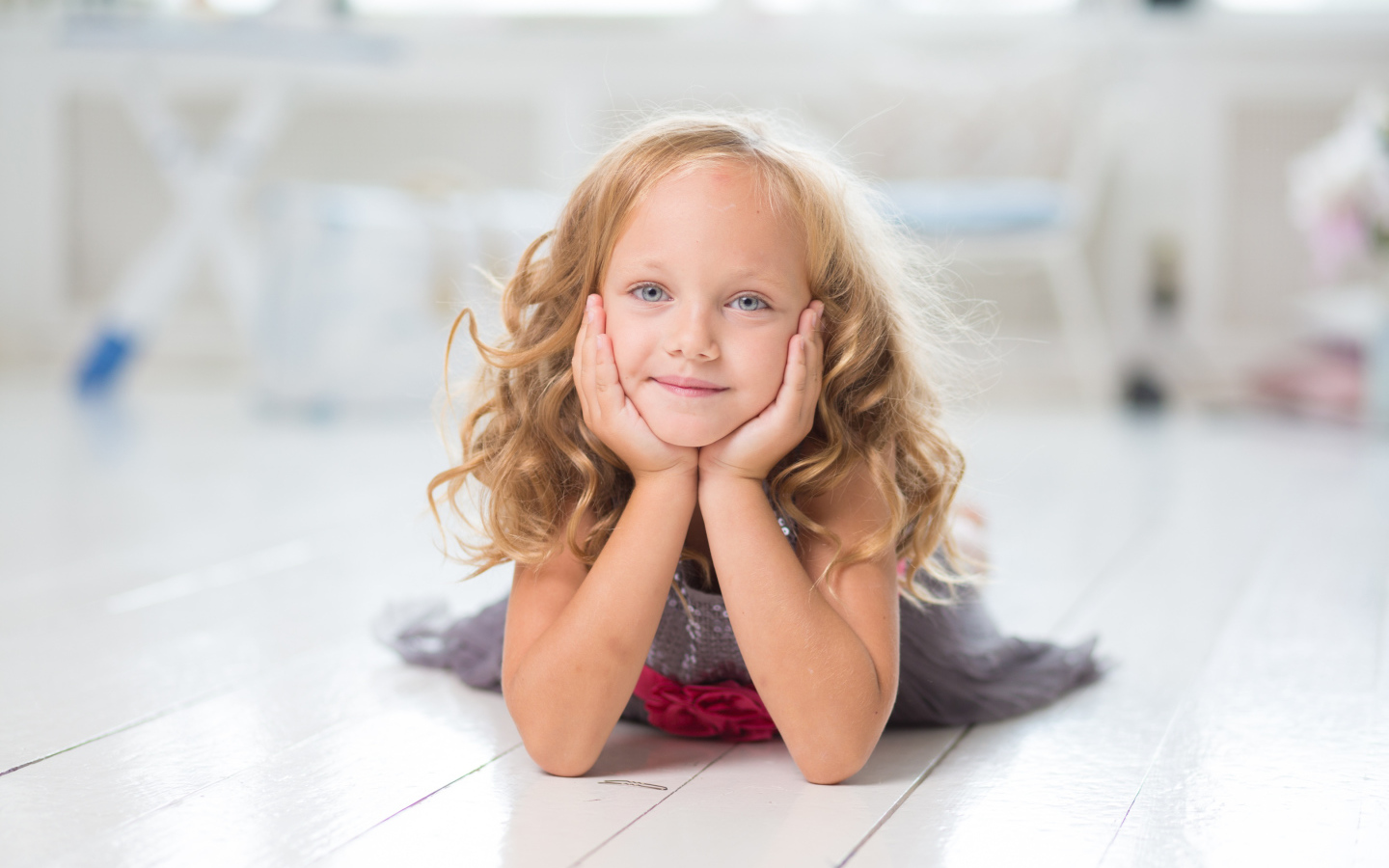 Маленькая длинноволосая голубоглазая девочка лежит на полу