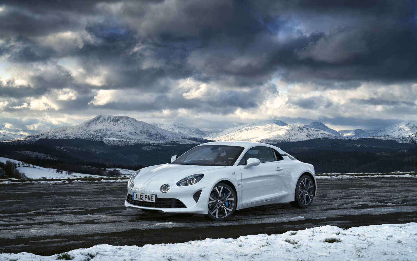 Белый автомобиль Alpine A110 на фоне гор под грозовым небом  