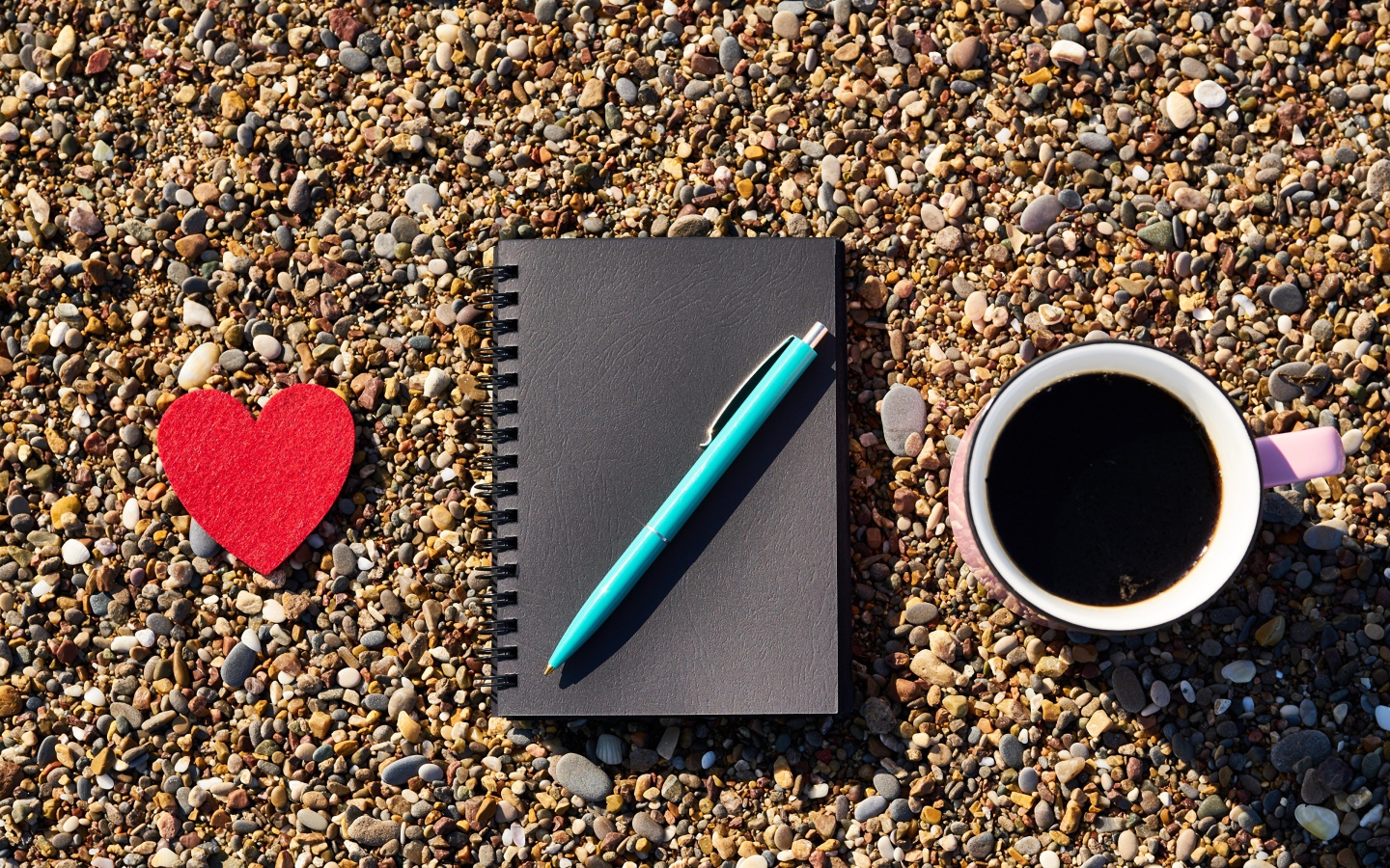 Блокнот с ручкой лет на мелкой гальке с чашкой кофе и красным сердцем 