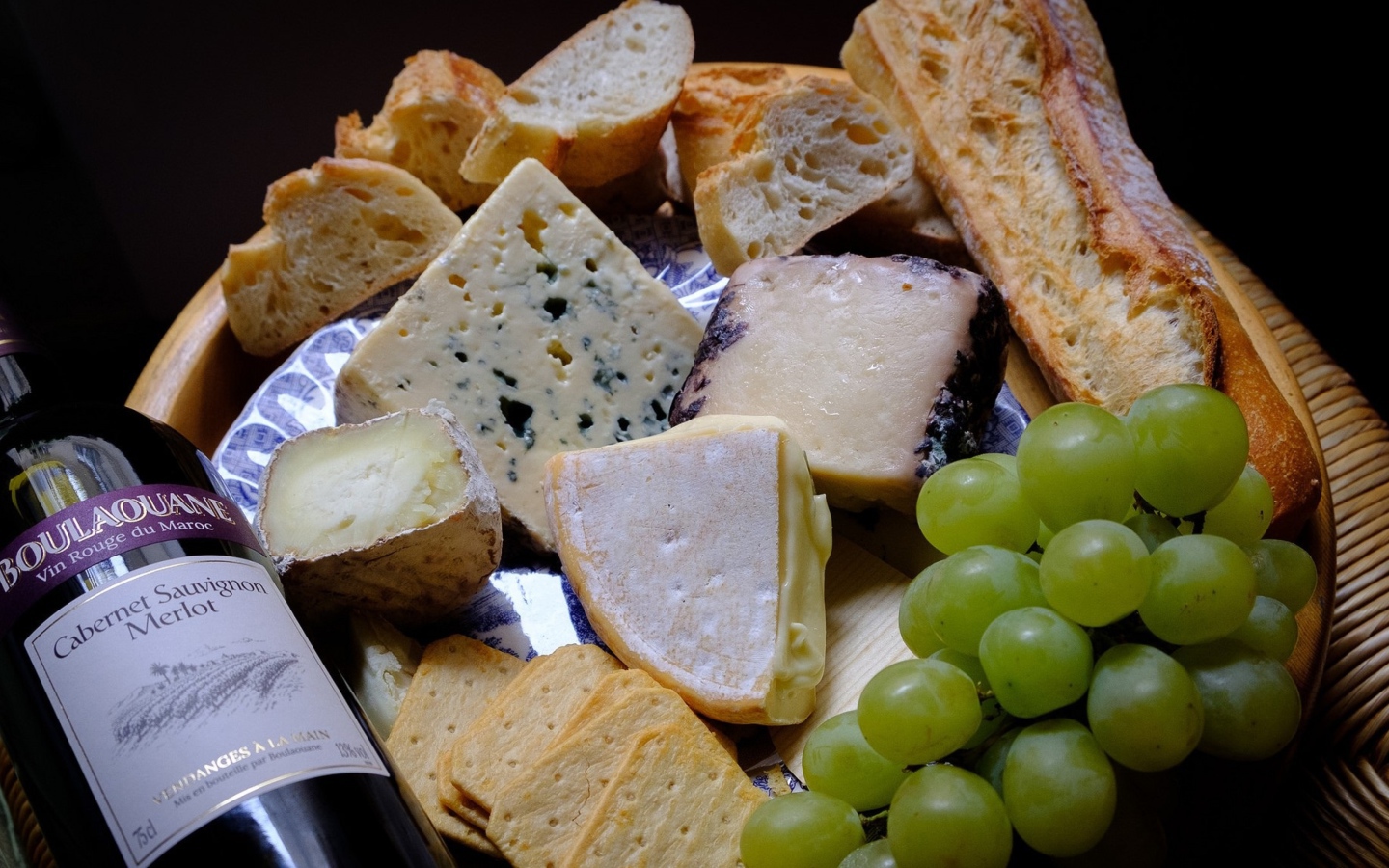 Разные виды твердого сыра на тарелке с белыми виноградом и вином