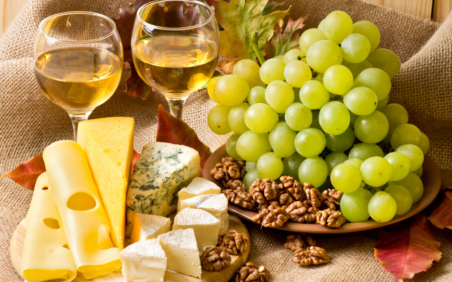 Белое вино на столе с сыром, виноградом и орехами