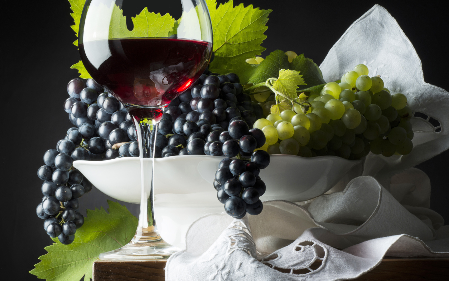 Бокал красного вина на столе с белым и синим виноградом