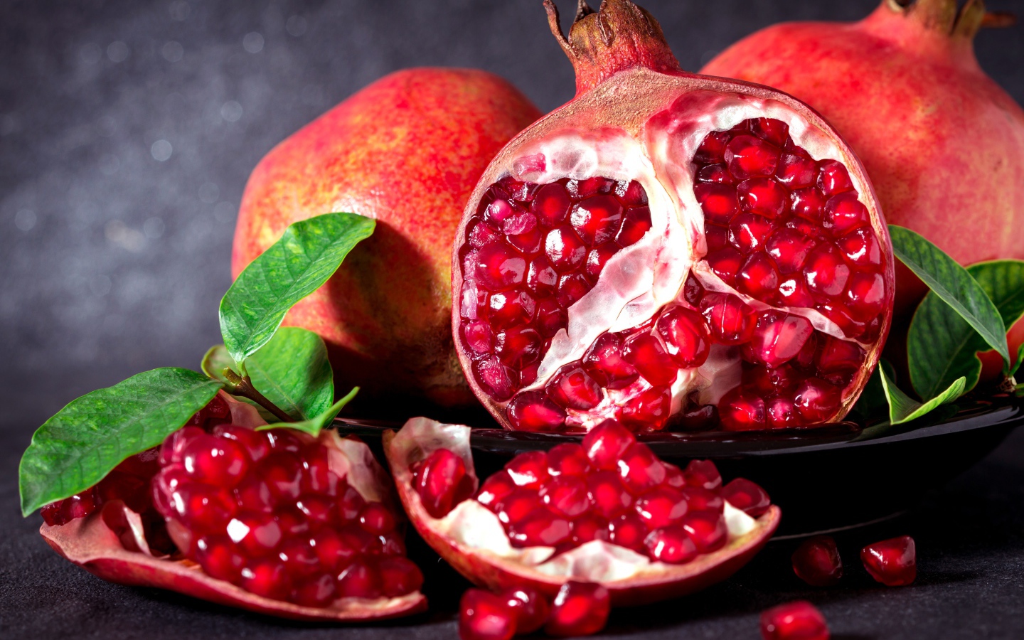 Красные гранаты с зернами и зелеными листьями на сером фоне