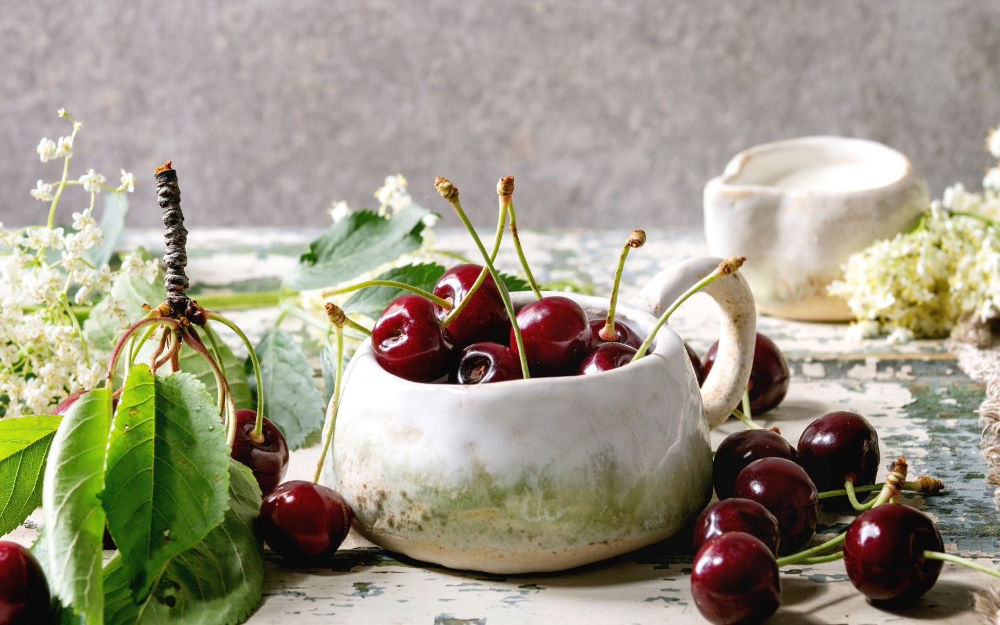 Спелые красные черешни на столе в белом чайнике