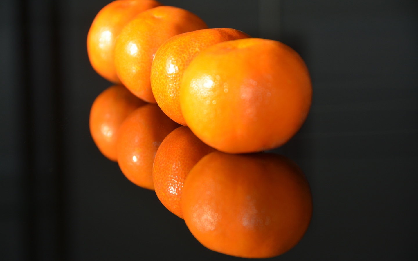 Желтые мандарины отражаются в поверхности стола 