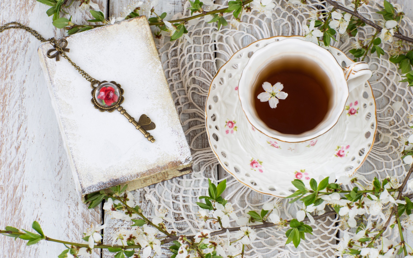Чашка чая на столе с книгой и белыми цветами вишни 