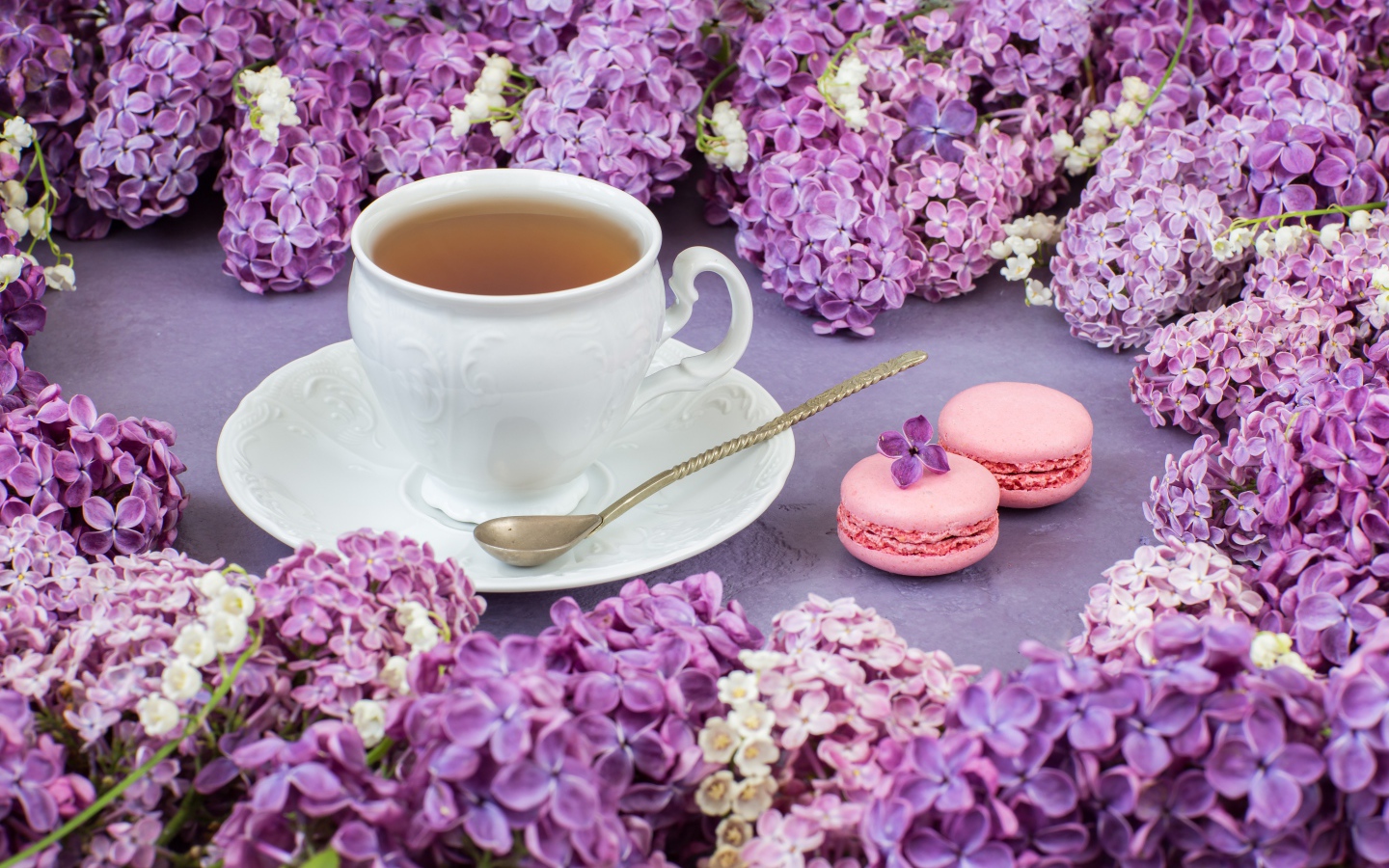 Чашка чая на столе с цветами сирени и десертом макарон