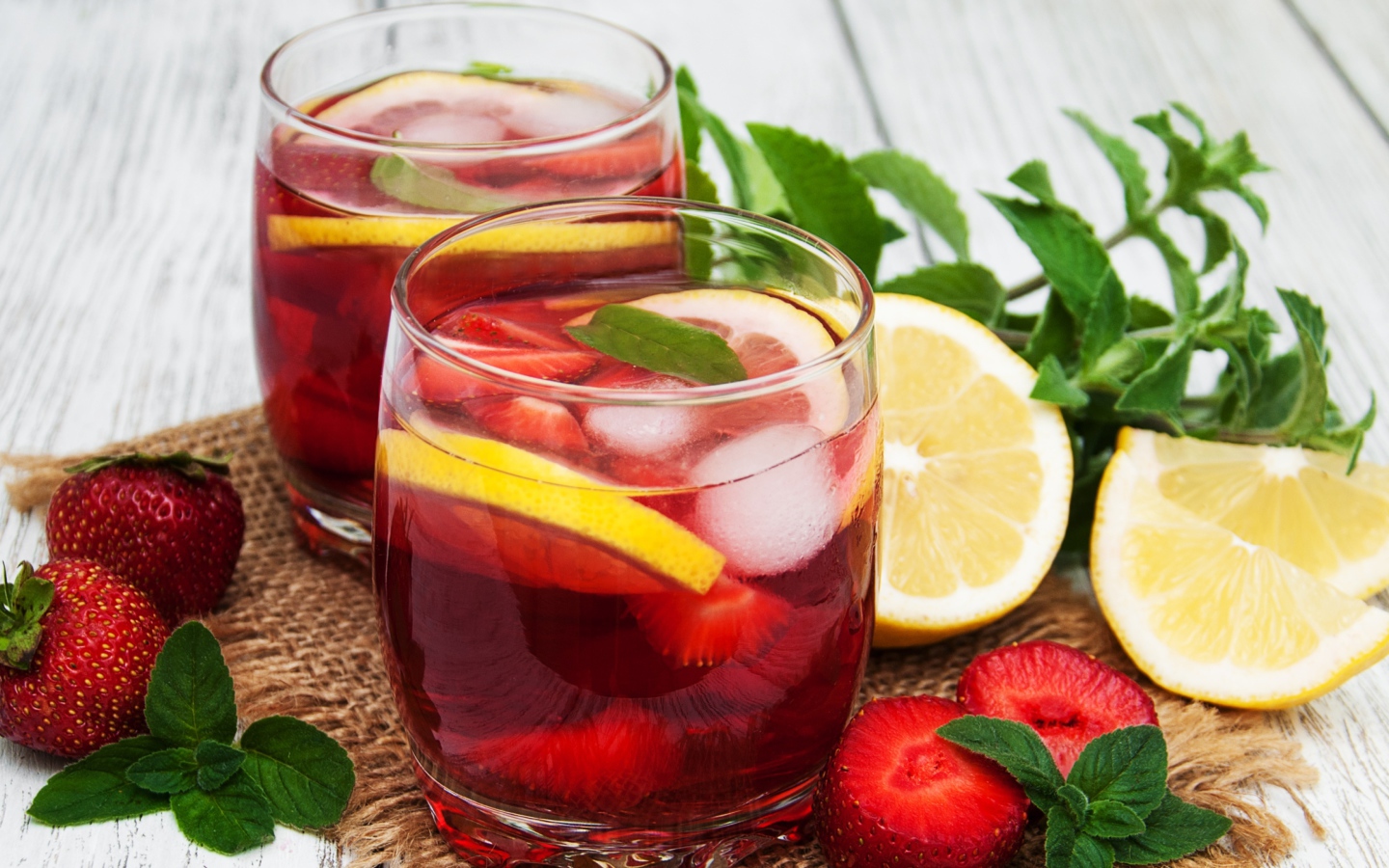 Мохито в стаканах на столе с клубникой, лимоном и мятой