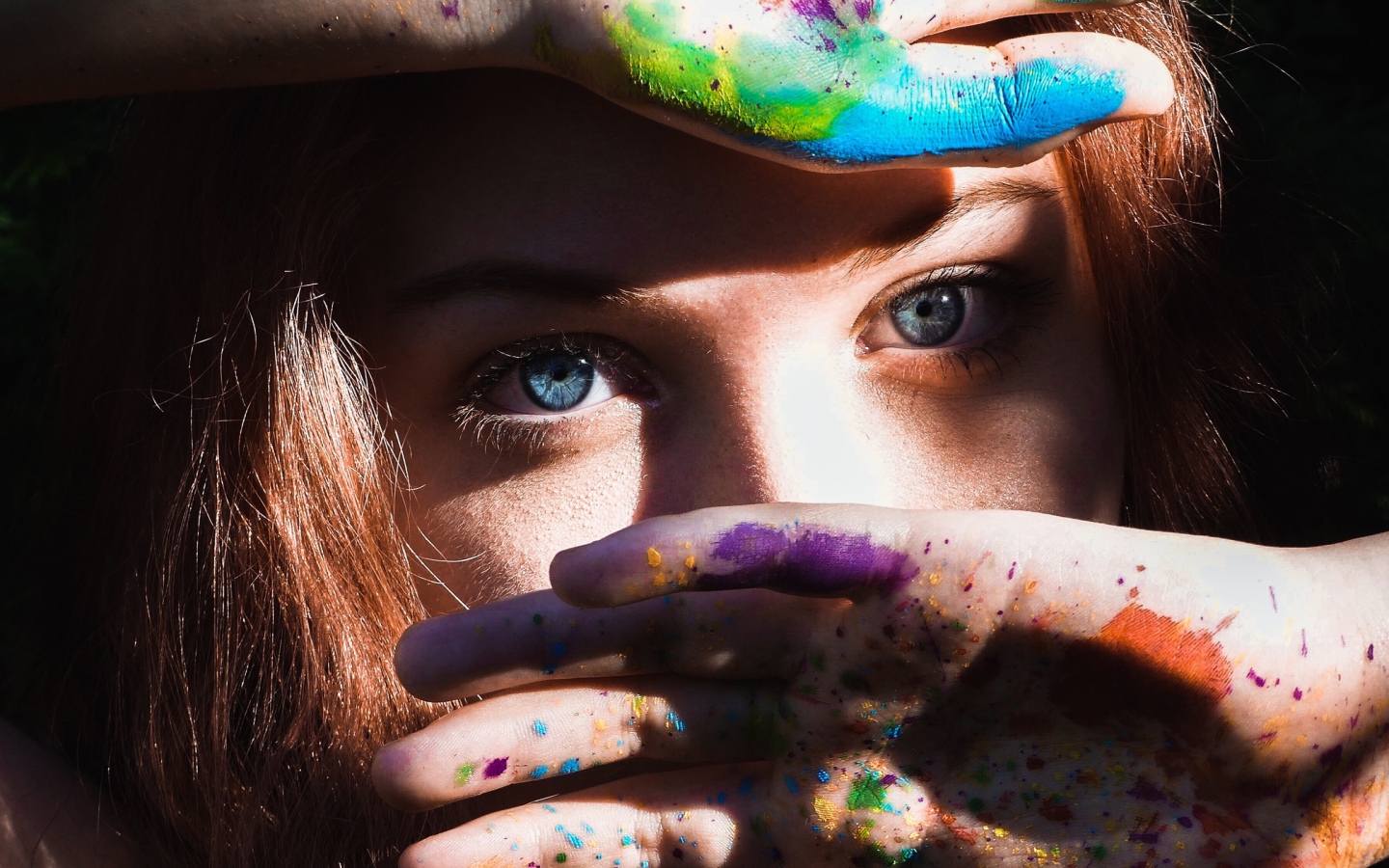 Красивая голубоглазая девушка с руками в разноцветной краске у лица