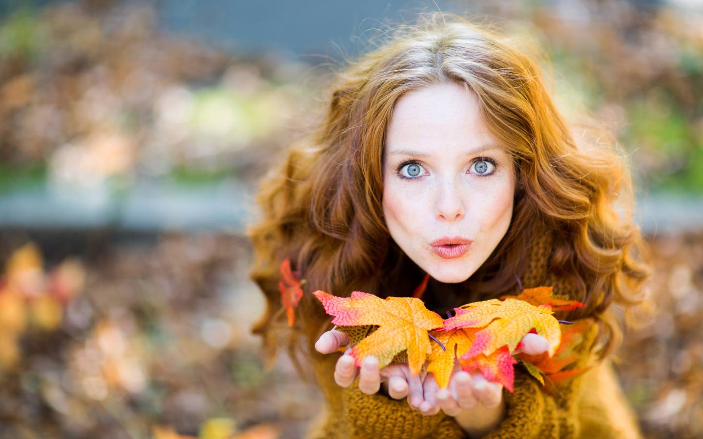 Красивая девушка сдувает листья с ладоней