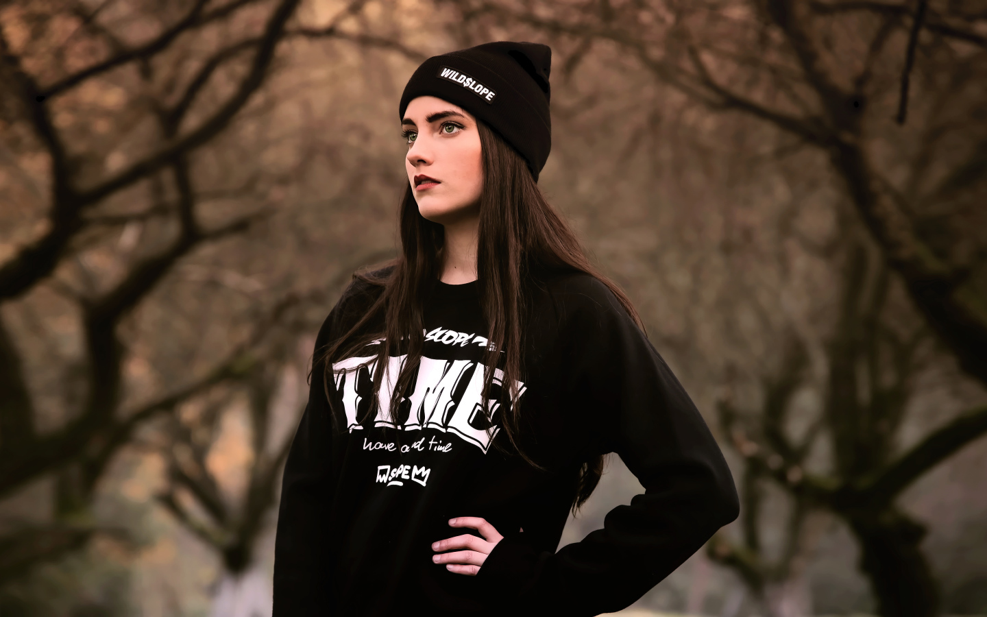 Красивая девушка в черной шапке у деревьев 