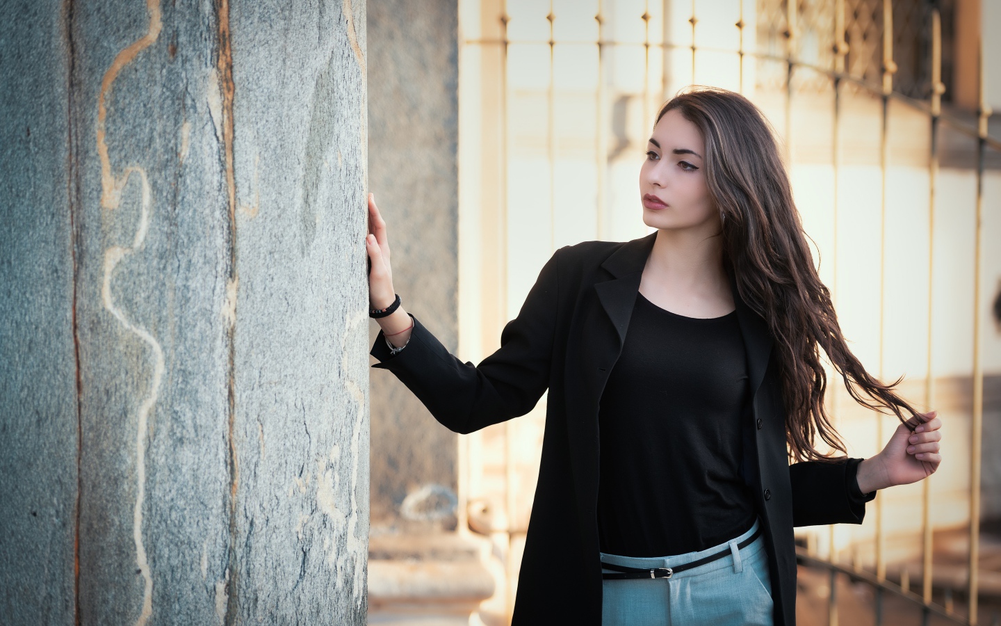 Красивая девушка в черном пиджаке стоит у стены