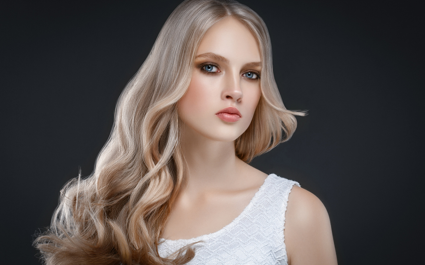 Красивая длинноволосая блондинка с голубыми глазами на сером фоне