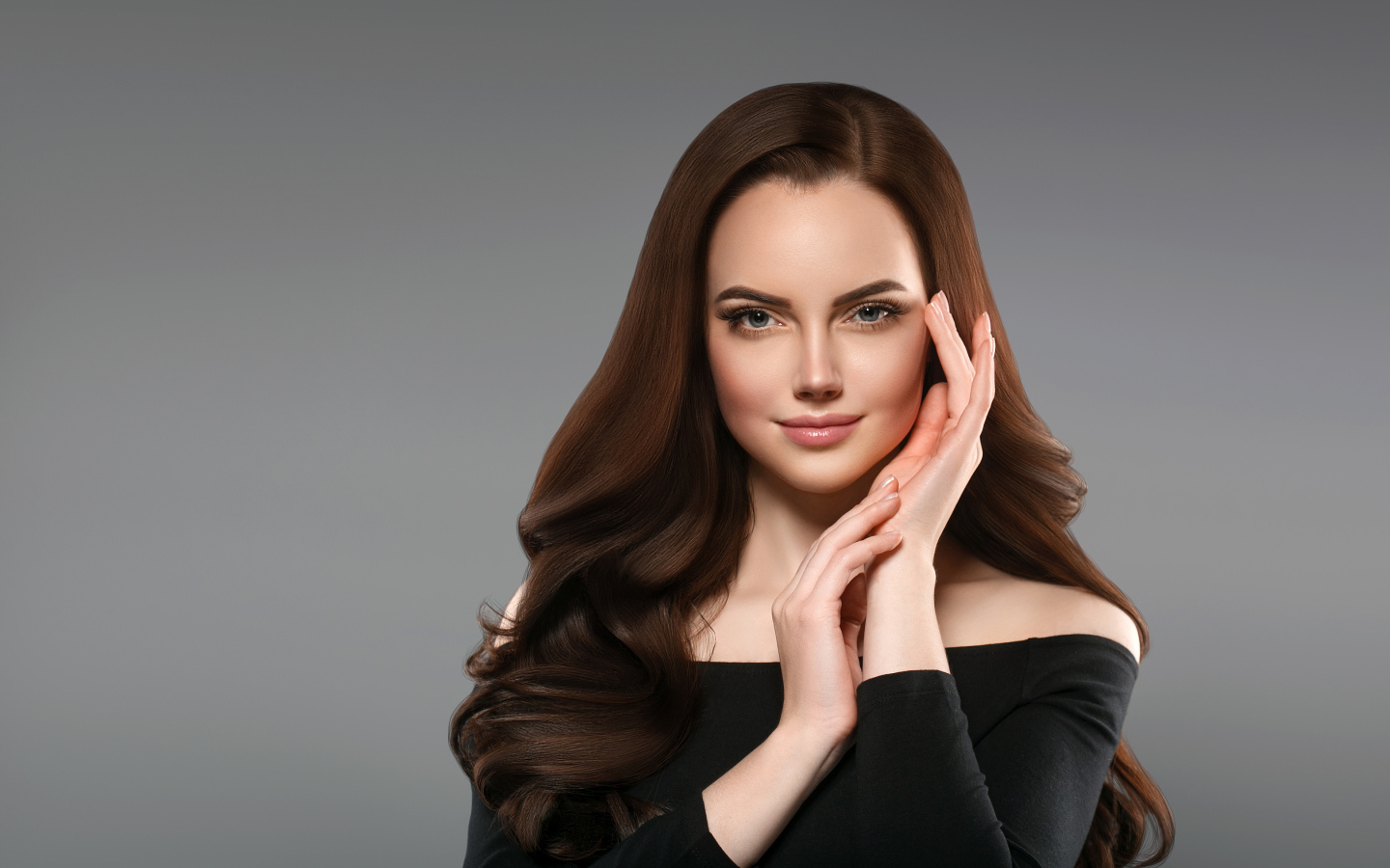 Красивая нежная длинноволосая шатенка  с руками у лица на сером фоне
