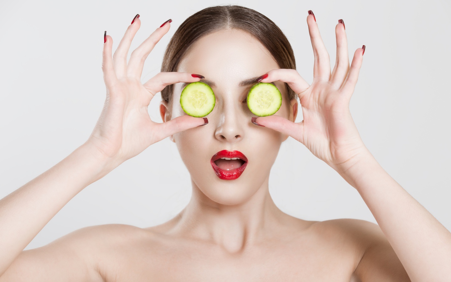 Яркая девушка с огурцами у глаз на сером фоне