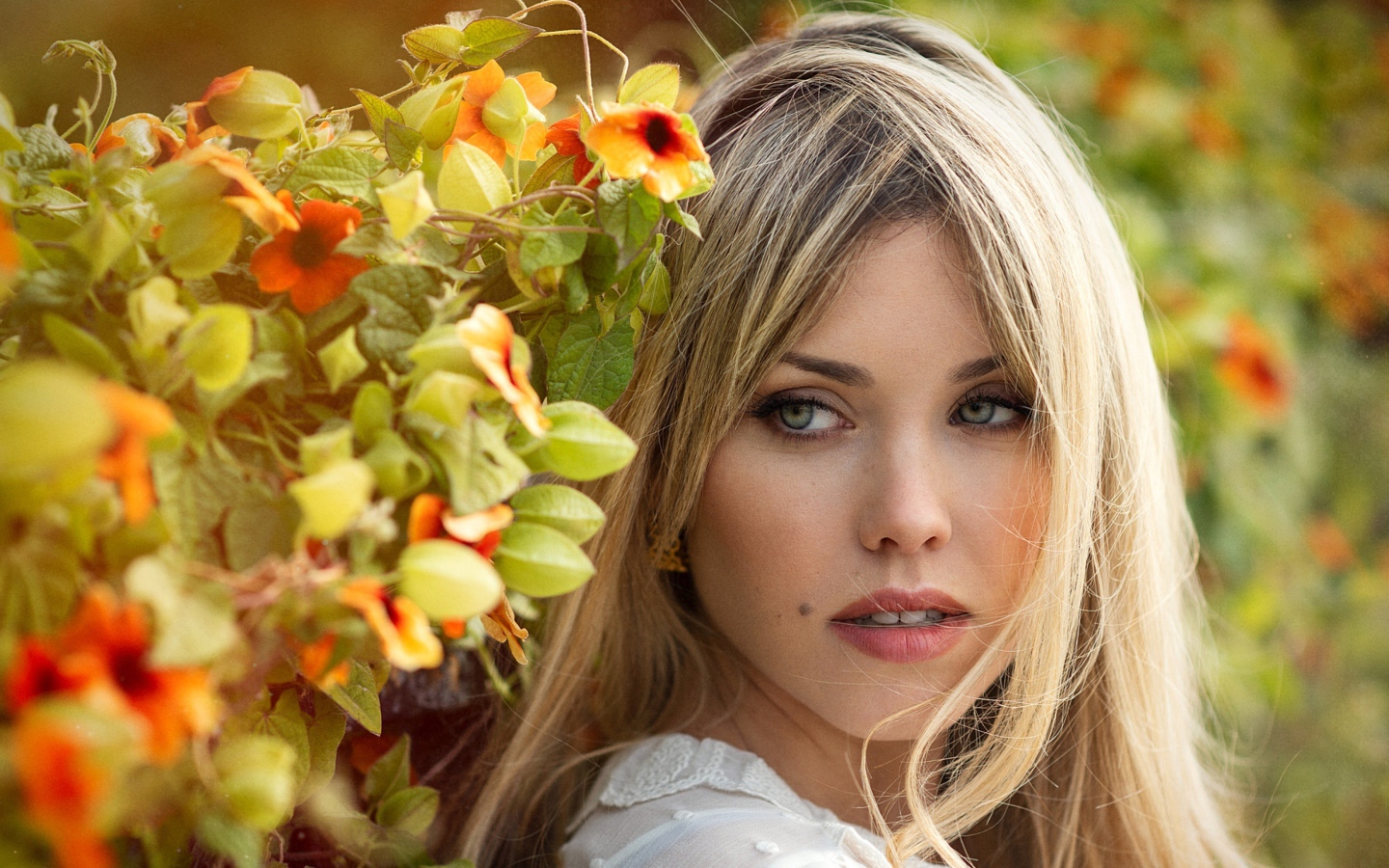 Зеленоглазая блондинка у забора с цветами 