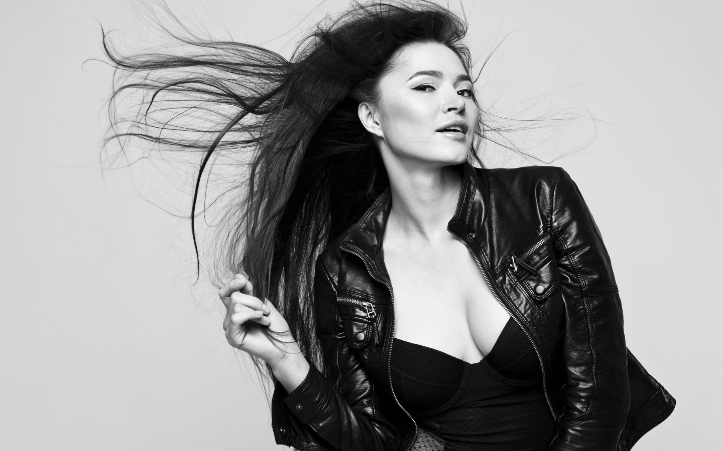 Длинноволосая брюнетка с кожаной куртке на сером фоне