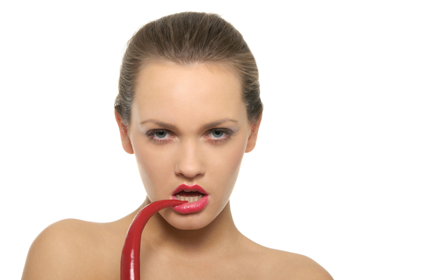 Молодая девушка кусает красный перец на белом фоне