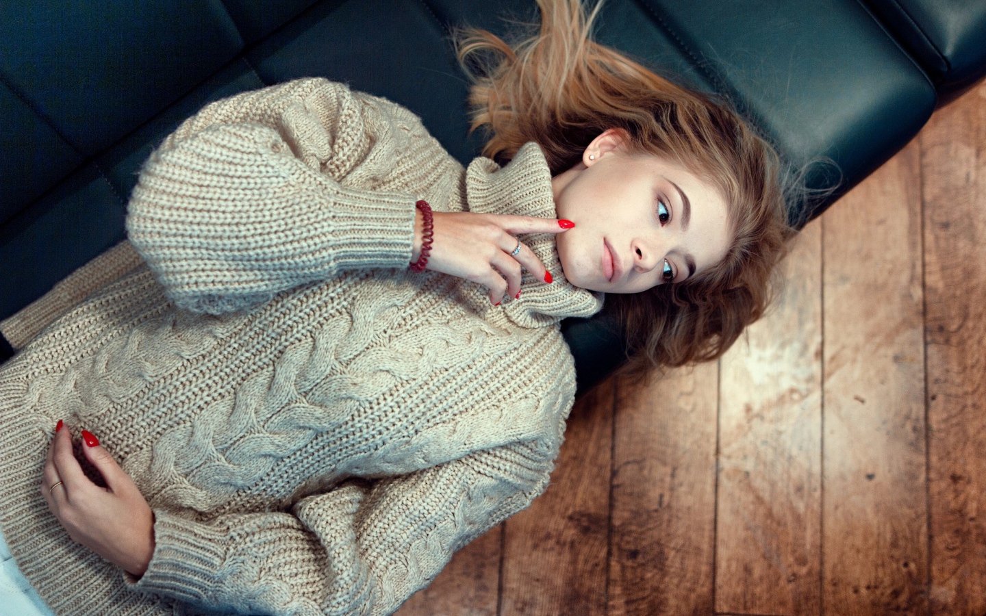 Молодая девушка в вязаном свитере лежит на черном кожаном диване