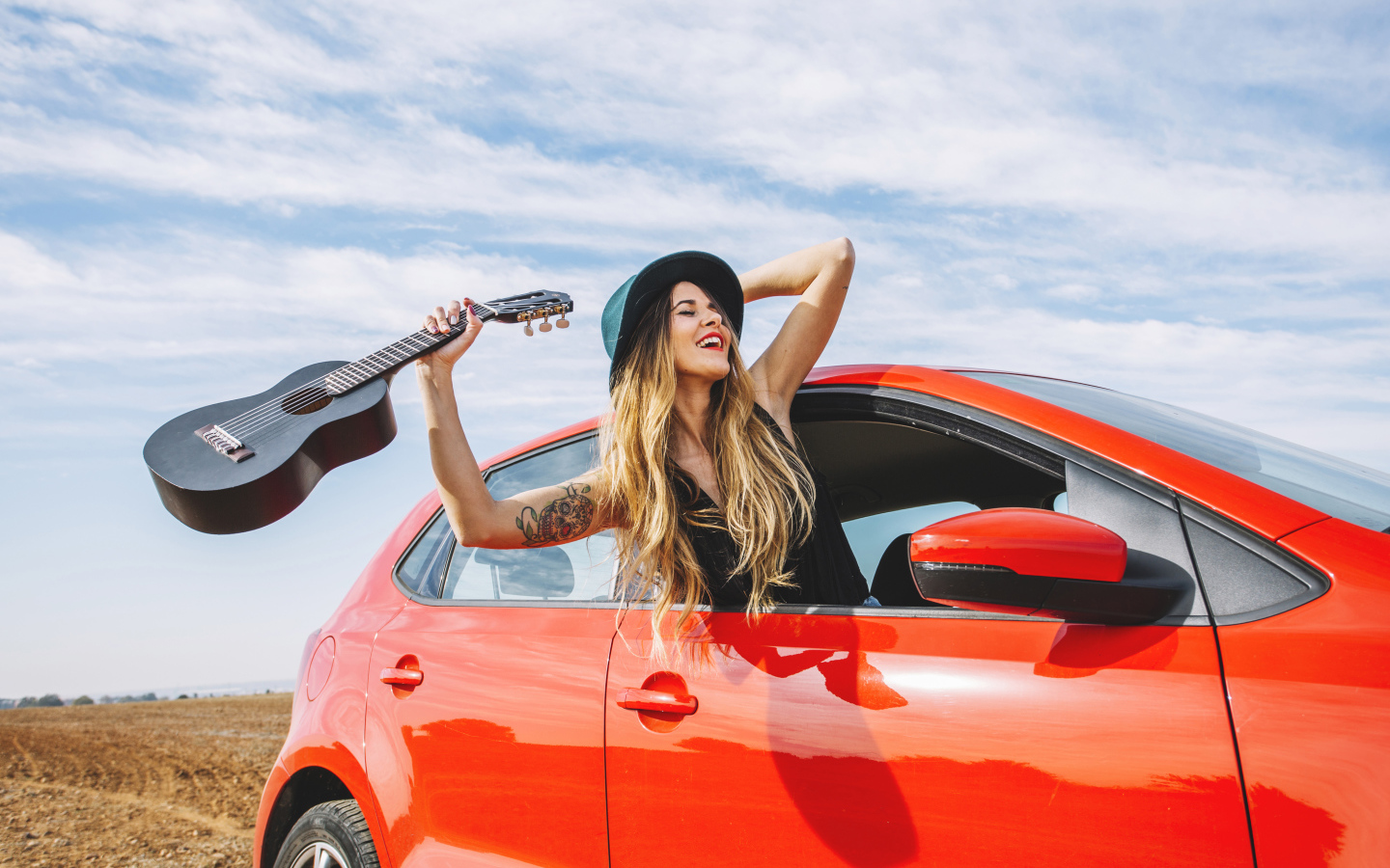 Молодая девушка с гитарой в красной машине летом