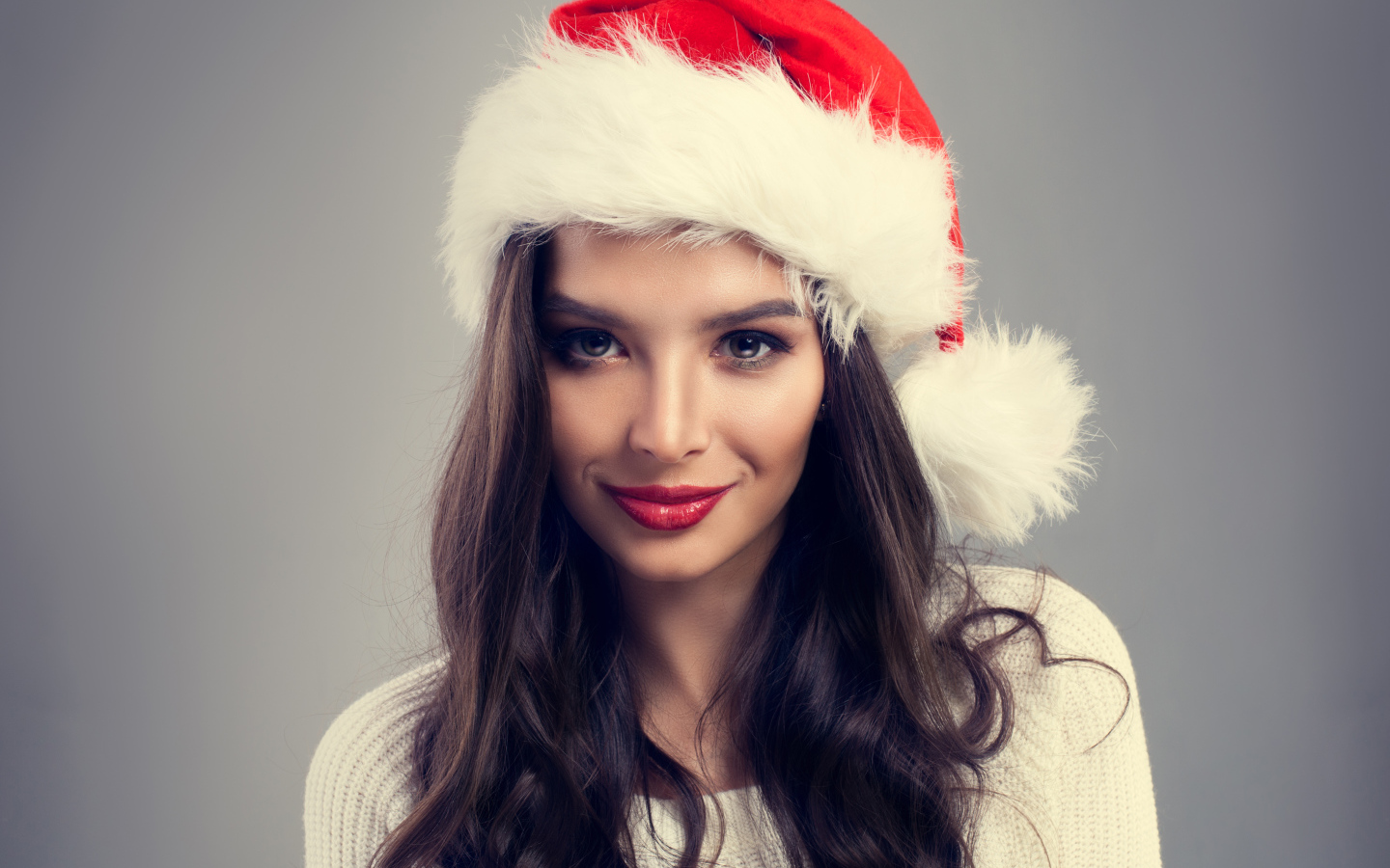 Beautiful brunette in santa hat on gray background