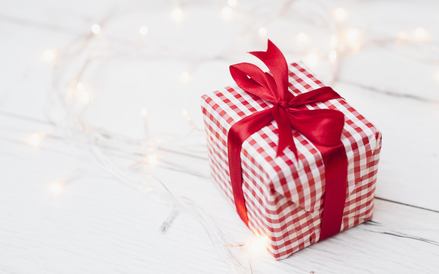 Подарок с красной лентой лежит на столе с гирляндой 